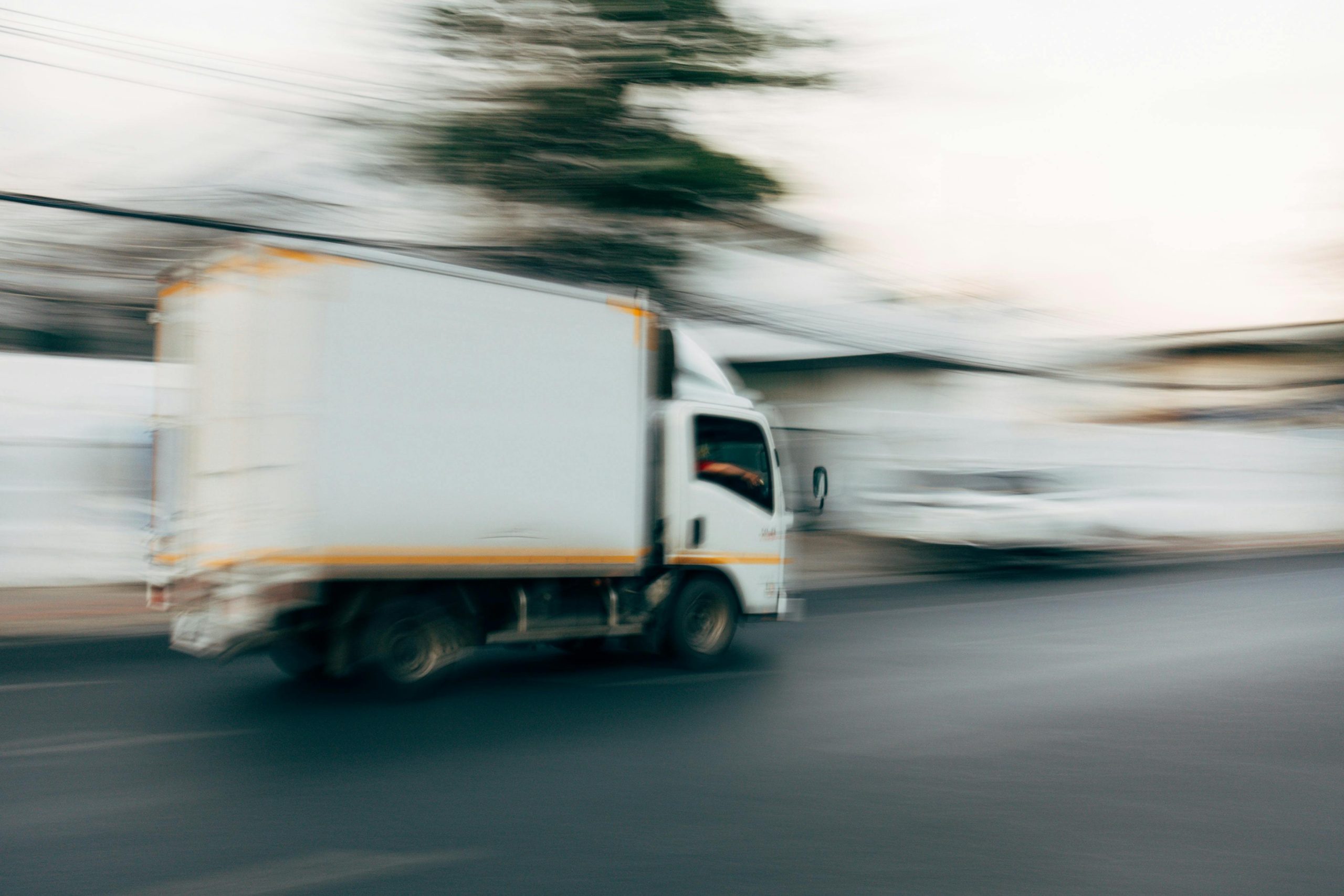 Blurred image of a truck speeding on a city road, capturing motion and urban life.